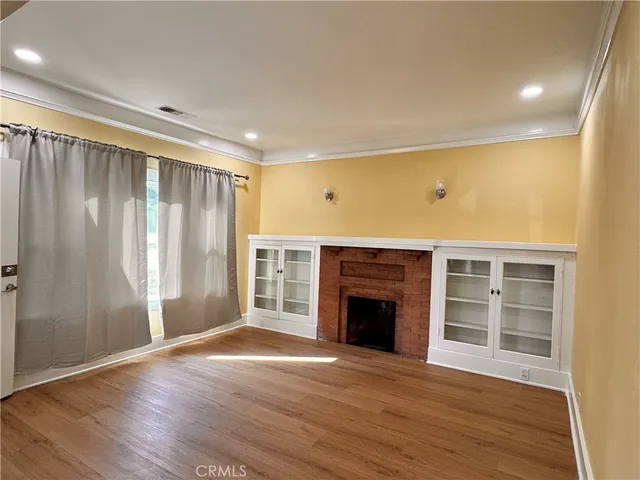 an empty room with wooden floor fireplace and windows