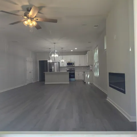 an empty room with wooden floor and kitchen view