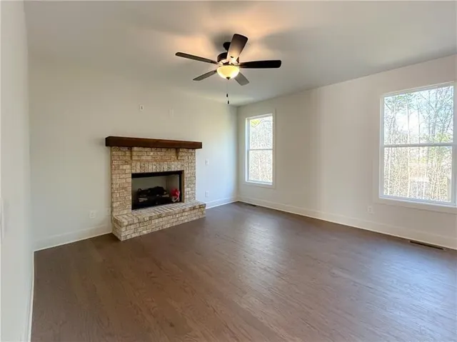 a view of an empty room with wooden floor fireplace and a window