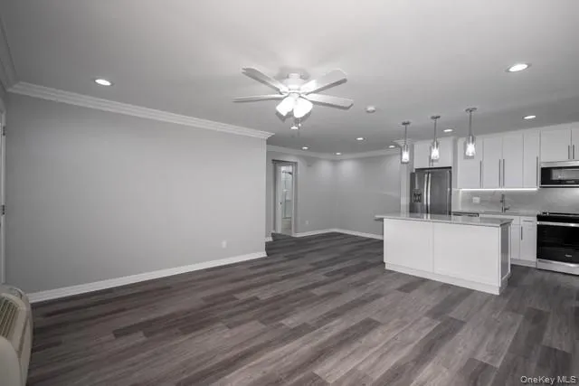 a view of an empty room and kitchen with wooden floor