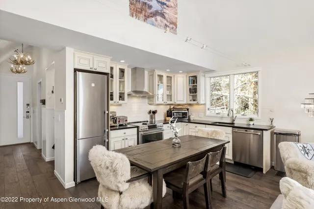 a kitchen with stainless steel appliances granite countertop a stove a refrigerator a sink a dining table and chairs