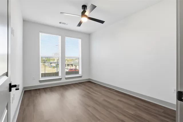 an empty room with wooden floor fan and windows