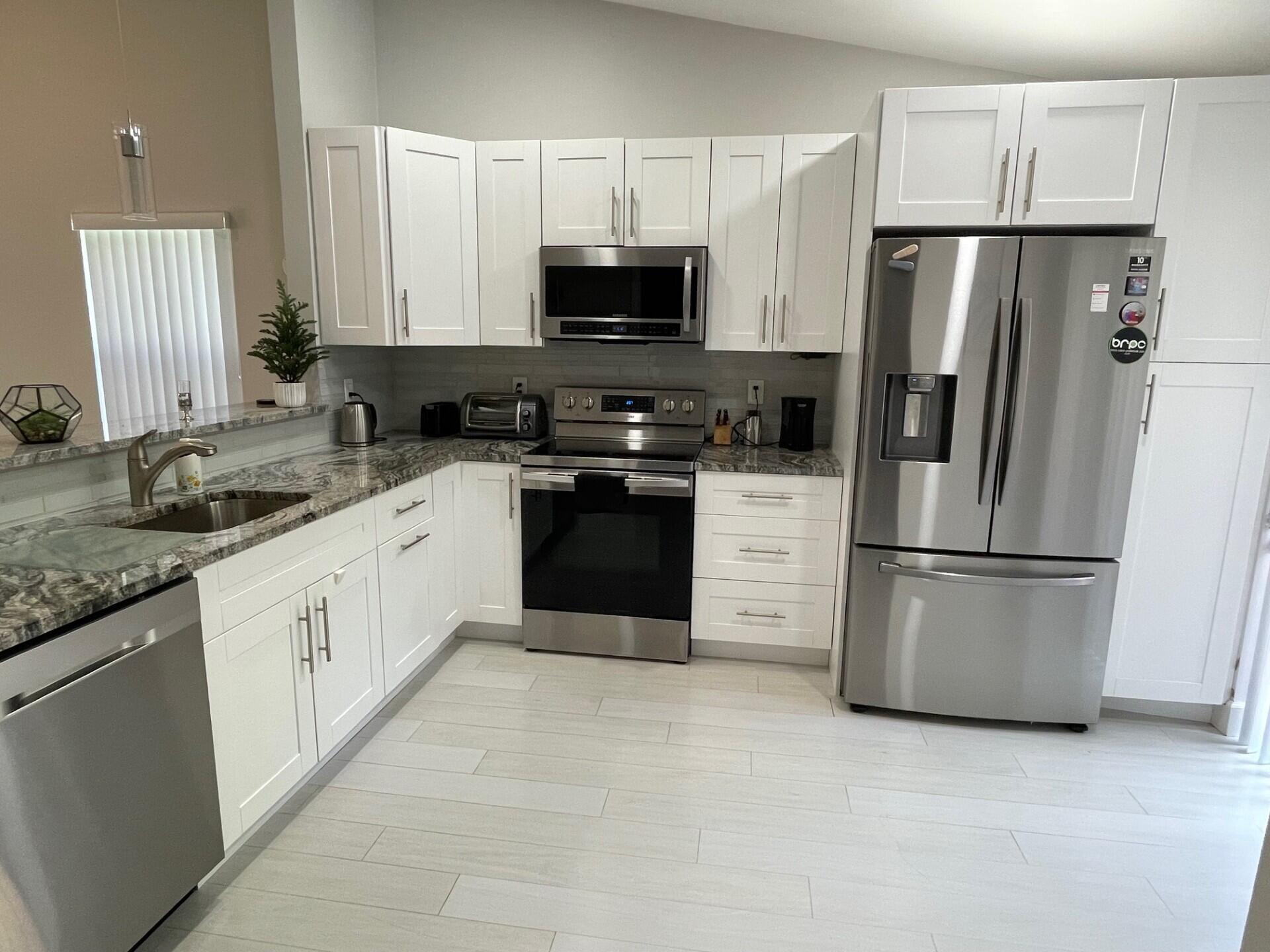 8471 Boca Glades Boulevard East Boca Raton, FL 33434 - Photo 11 of 29 a kitchen with stainless steel appliances granite countertop a refrigerator stove a sink and a microwave