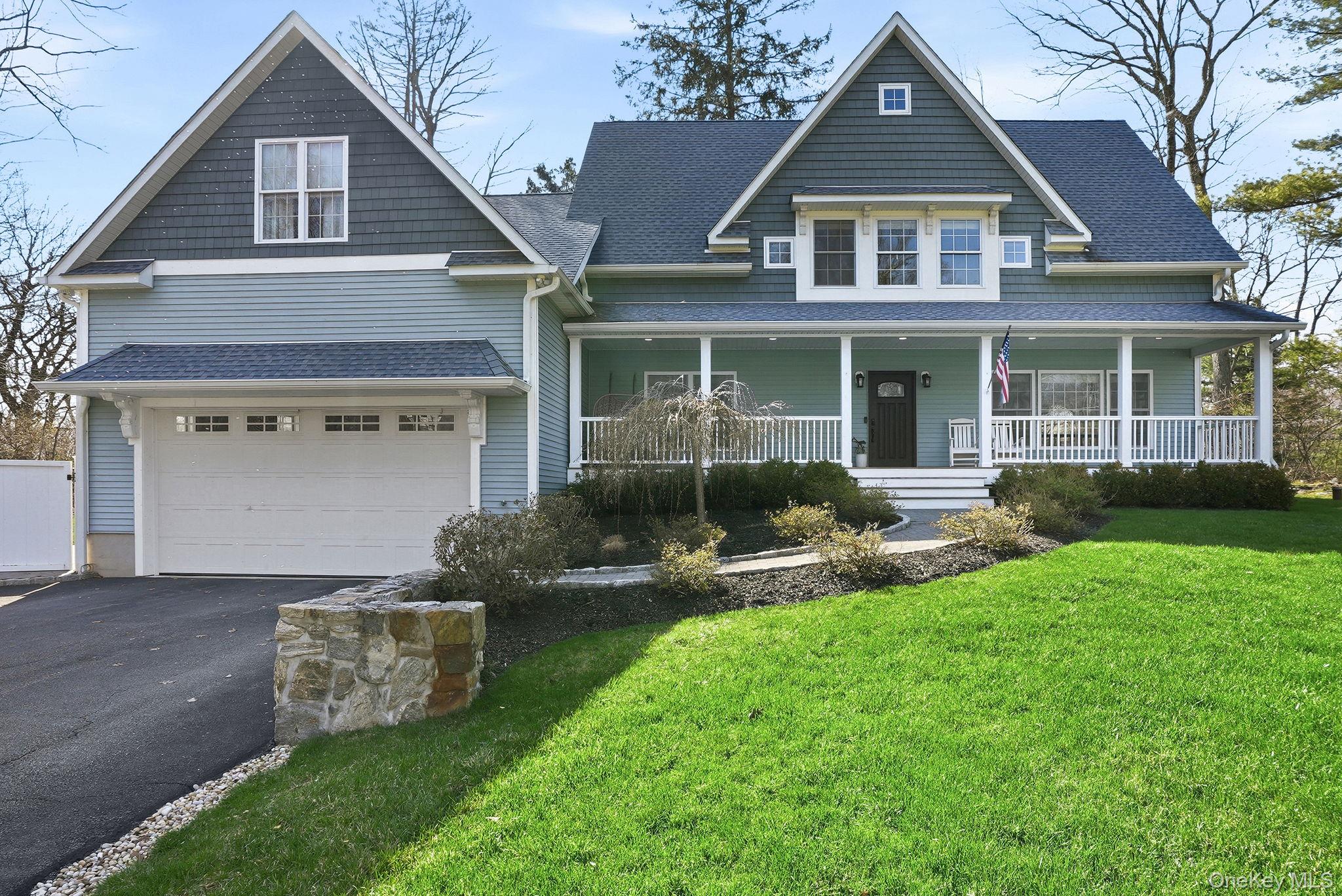 View of front of house with covered porch, an attached garage, driveway, a front lawn, and roof with shingles