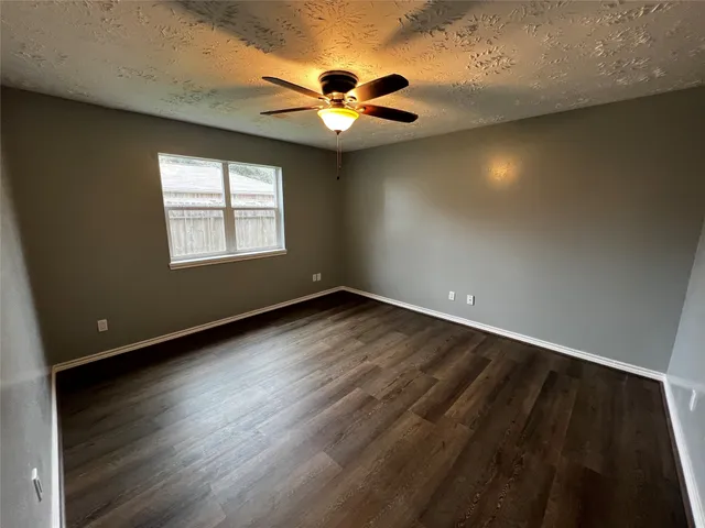 an empty room with wooden floor fan and windows