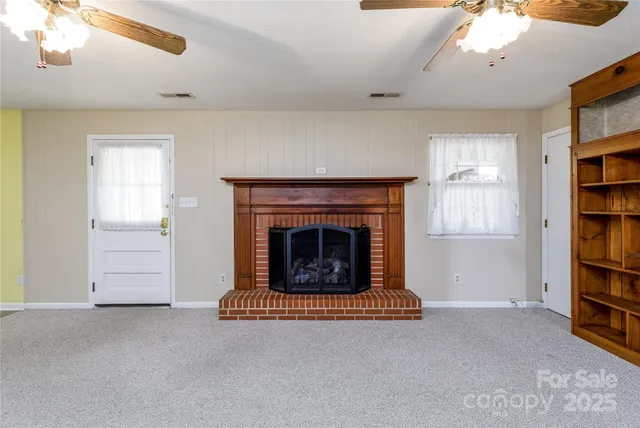 an empty room with fireplace chandelier fan and windows