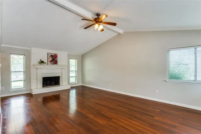a view of an empty room with wooden floor fireplace and a window
