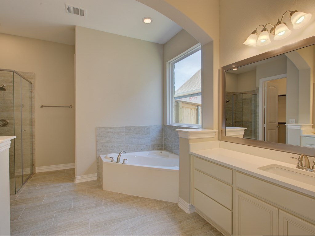 4303 Logan Ridge Drive Cedar Park, TX 78613 - Photo 11 of 24 Bathroom featuring a corner soaking tub with tile surround, a separate glass-enclosed shower, dual vanity with undermount sinks and light countertops, a framed mirror, and recessed lighting