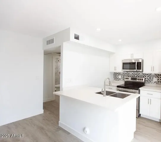 a kitchen with stainless steel appliances a sink a stove a microwave a sink and white cabinets