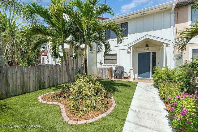 a view of a white house with a small yard plants and a large tree