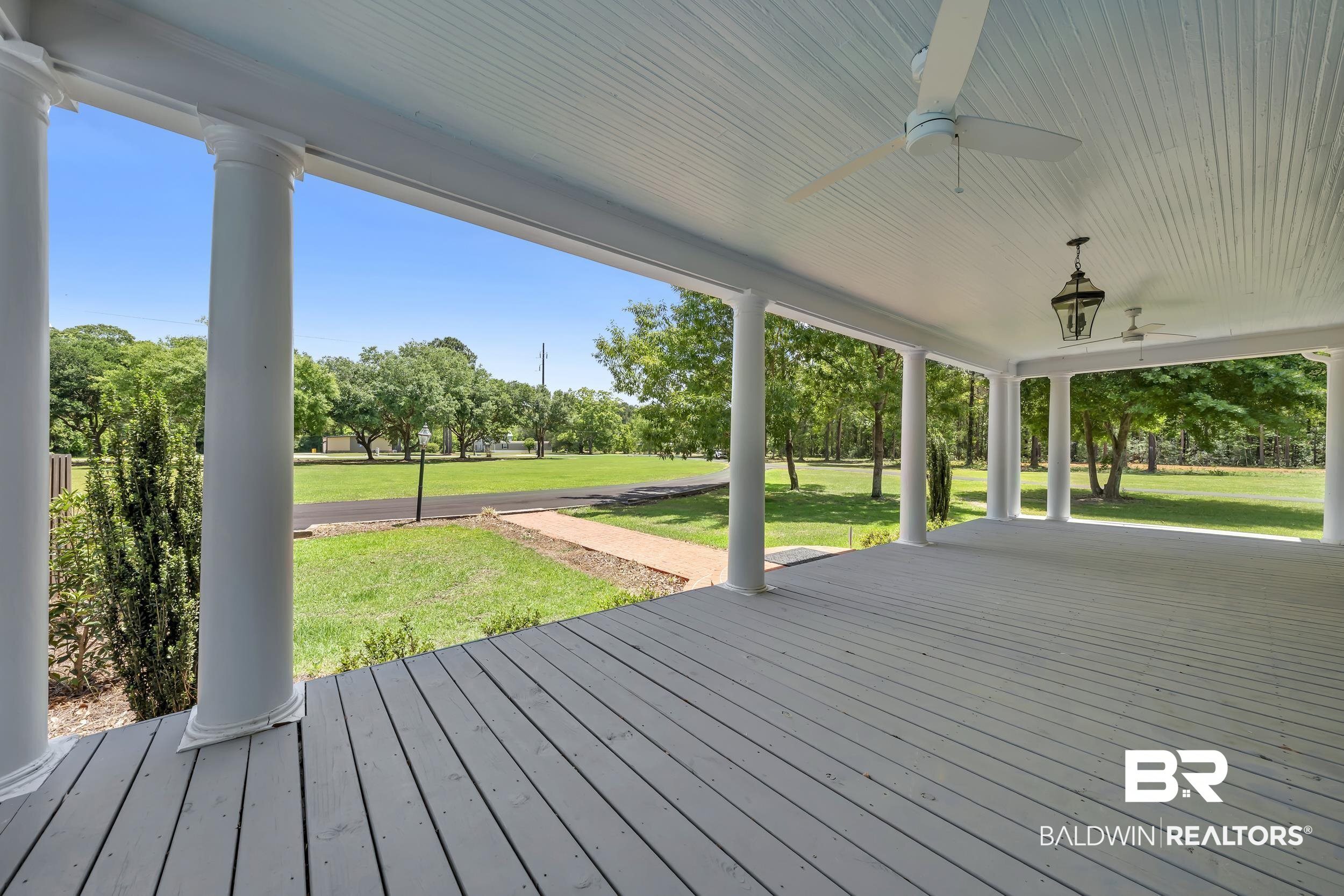 43199 Pine Grove Road Bay Minette, AL 36507 - Photo 29 of 71 Expansive covered porch featuring a painted wood-plank floor, architectural columns, beadboard ceiling, two ceiling fans, and an exterior lantern fixture