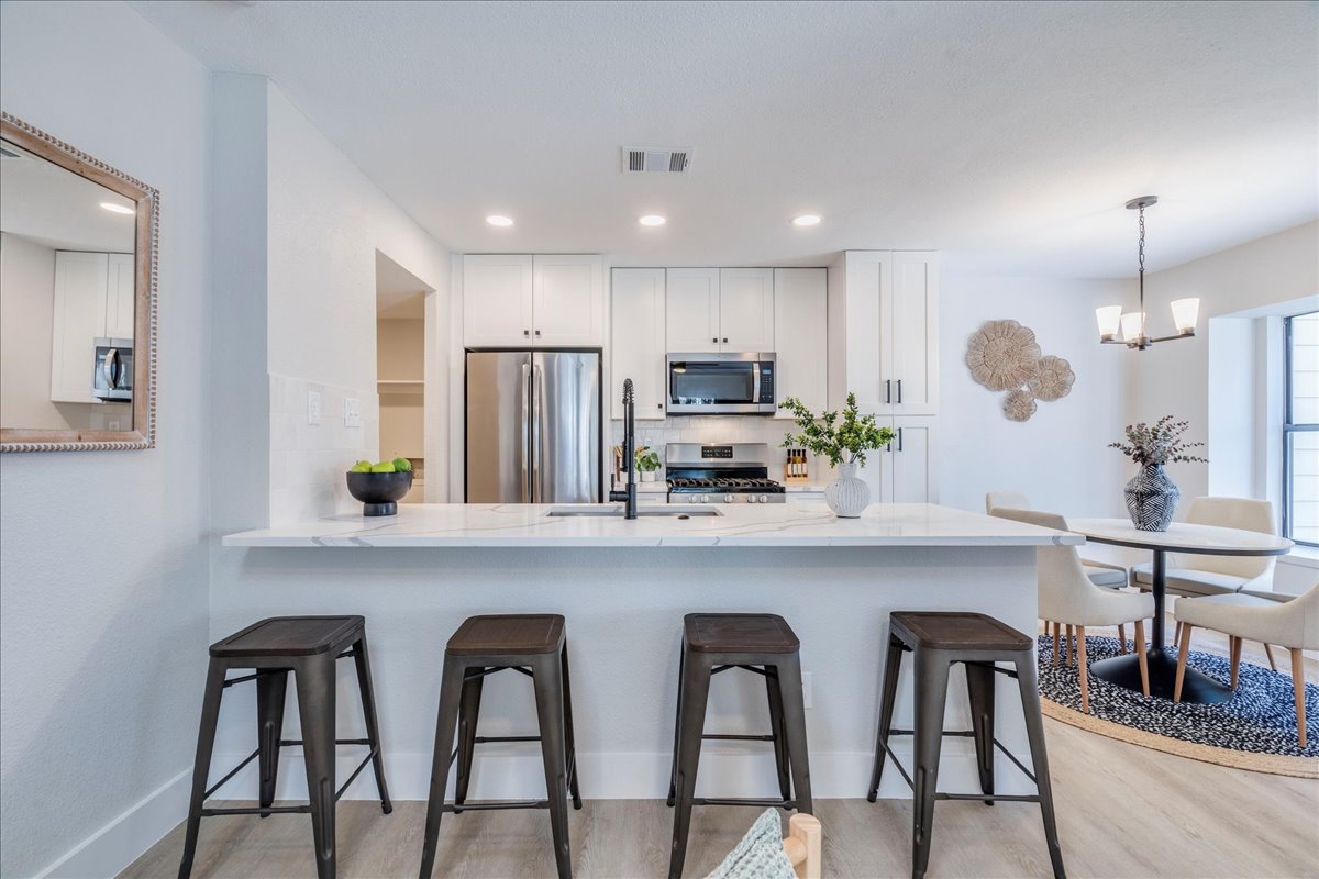 11301 Jollyville Road, Unit F2 Austin, TX 78759 - Photo 1 of 1 Kitchen featuring white cabinetry, light stone countertops, stainless steel appliances, decorative light fixtures, and a breakfast bar