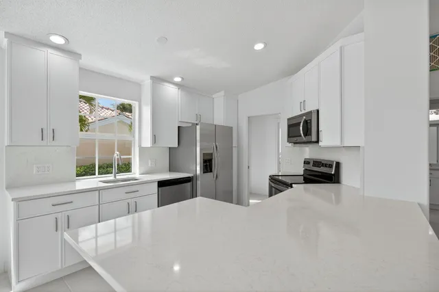a large white kitchen with granite countertop a stove a sink a window and stainless steel appliances