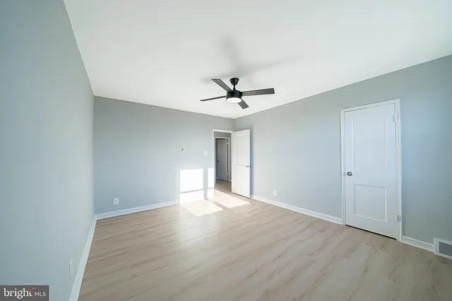 a view of an empty room with wooden floor and a ceiling fan