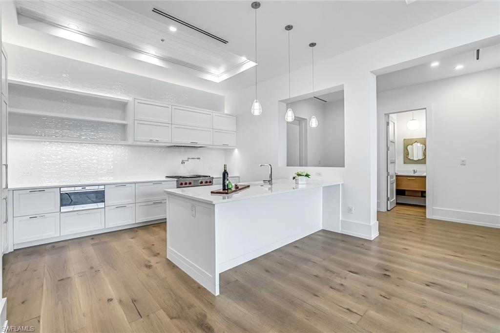 201 8th Street South, Unit 308 Naples, FL 34102 - Photo 3 of 28 a large white kitchen with kitchen island a sink a stove and wooden floors