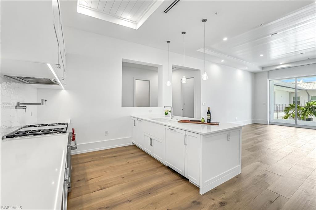 201 8th Street South, Unit 308 Naples, FL 34102 - Photo 6 of 28 a large white kitchen with a stove a sink a refrigerator and a dining table with wooden floor