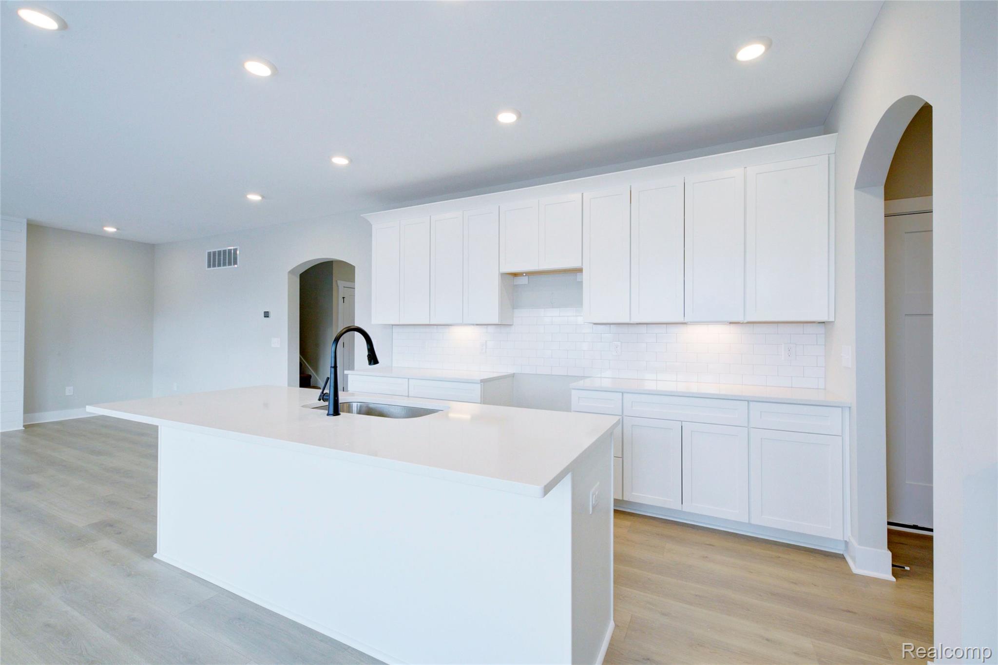 579 Round Rock (moh80) Howell, MI 48843 - Photo 6 of 42 Kitchen with arched walkways, white cabinets, an island with sink, light stone countertops, and light wood-style floors