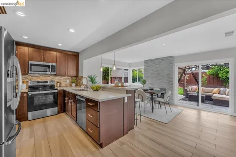 a kitchen with stainless steel appliances granite countertop a stove top oven a sink dishwasher a dining table and chairs with wooden floor