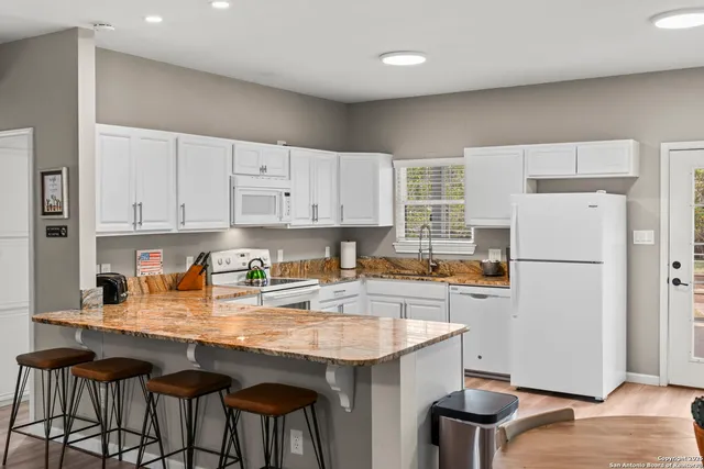 a kitchen with granite countertop a refrigerator a stove a sink dishwasher and white cabinets with wooden floor