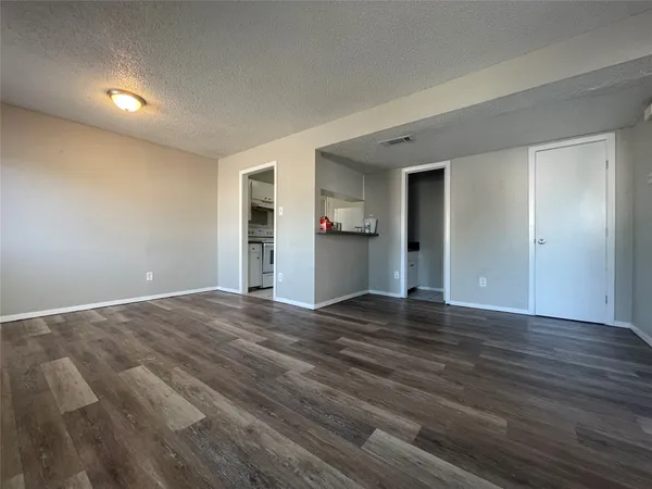 a view of an empty room with wooden floor and kitchen space