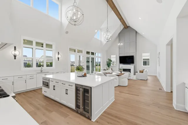 a large white kitchen with a stove a sink dishwasher a dining table and chairs with wooden floor