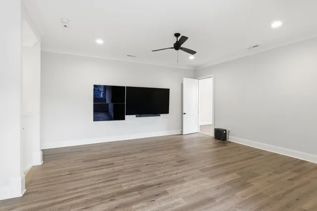 a view of an empty room with wooden floor and a ceiling fan