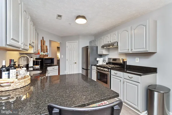a kitchen with stainless steel appliances kitchen island granite countertop a stove a sink a dining table and chairs with wooden floor