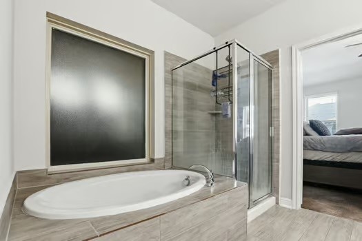 24714 Longwood Forest Drive Spring, TX 77373 - Photo 12 of 21 Modern bathroom with a sleek glass-enclosed shower and a spacious built-in bathtub. Neutral tile flooring and walls create a clean, contemporary look. Frosted window provides privacy while allowing natural light. Adjacent to a bedroom.