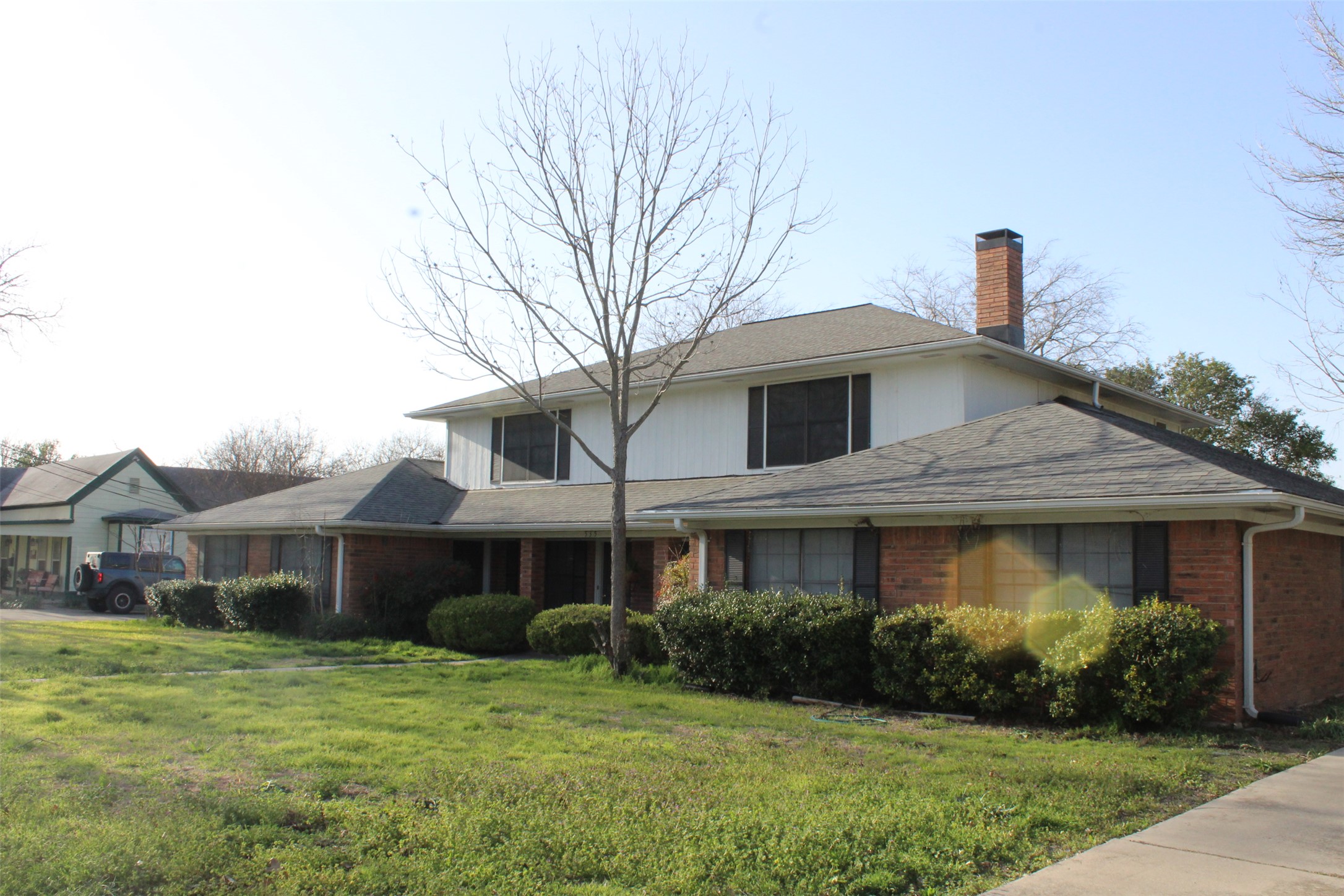 A well-maintained brick and white siding residence awaits, featuring a prominent chimney and mature landscaping.