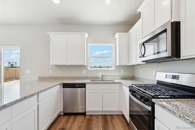 a white kitchen with stainless steel appliances granite countertop white cabinets granite counter tops and a wooden floor