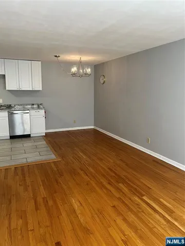 an empty room with wooden floor and kitchen view