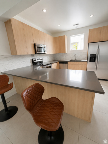 7750 Rooftop Drive Midvale, UT 84047 - Photo 2 of 8 Modern kitchen featuring an expansive island with a solid surface countertop, light wood-finish cabinetry, stainless steel appliances, a tile backsplash, and recessed lighting