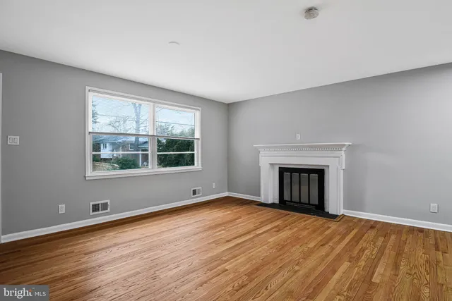 an empty room with wooden floor fireplace and windows