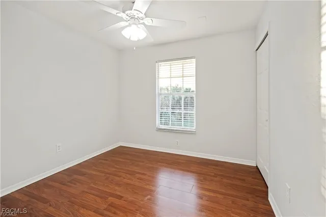 an empty room with wooden floor ceiling fan and windows