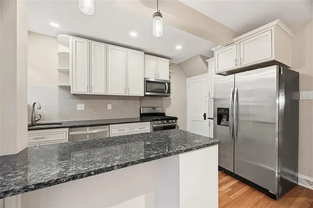 a kitchen with stainless steel appliances granite countertop a refrigerator a sink and white cabinets