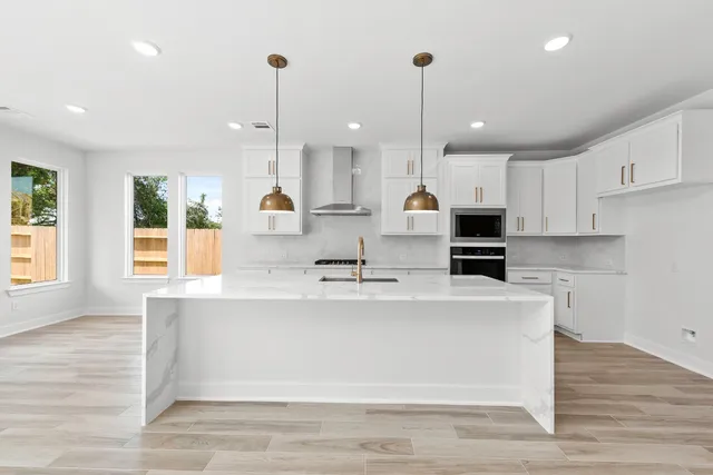 a large white kitchen with kitchen island a stove a sink a refrigerator and white cabinets with wooden floor