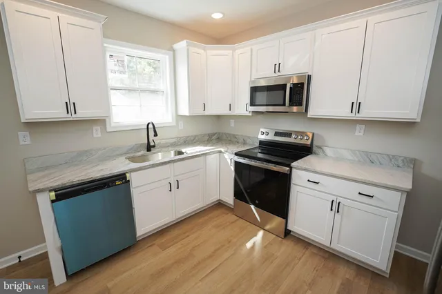 a kitchen with granite countertop white cabinets appliances a sink and a window