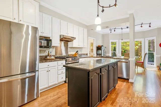 a kitchen with stainless steel appliances granite countertop a refrigerator a sink dishwasher a stove and a dining table with wooden floor