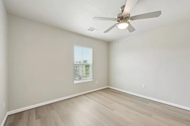 an empty room with wooden floor fan and windows