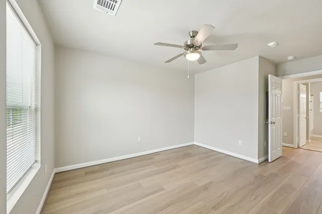 an empty room with wooden floor fan and windows