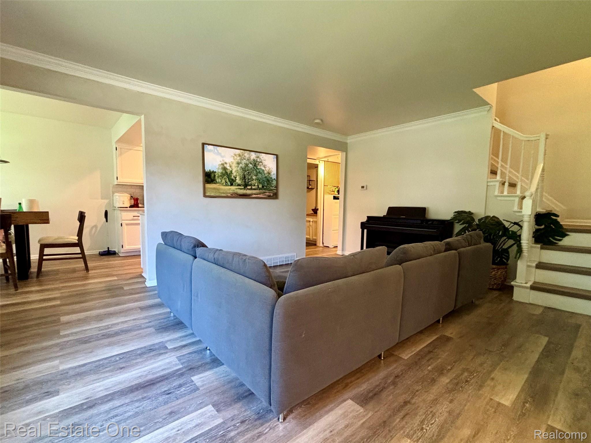 66 Meadow Wood Drive Rochester, MI 48307 - Photo 5 of 20 Open-concept living area featuring wood-finish flooring, white crown molding, and a staircase with white spindles and wooden treads