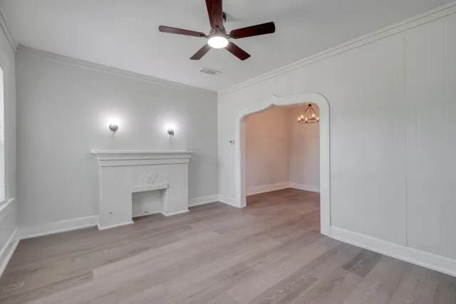 an empty room with wooden floor a ceiling fan a fireplace and windows
