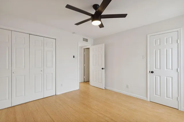 a view of an empty room with wooden floor and a ceiling fan