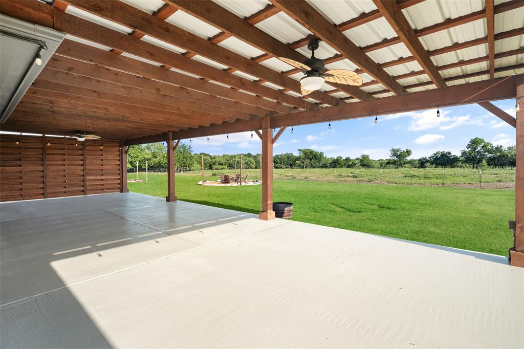 1019 Vaughan Lane Tioga, TX 76271 - Photo 31 of 40 Expansive covered patio featuring a wood-beam ceiling with corrugated metal roofing, an integrated ceiling fan, and string lighting