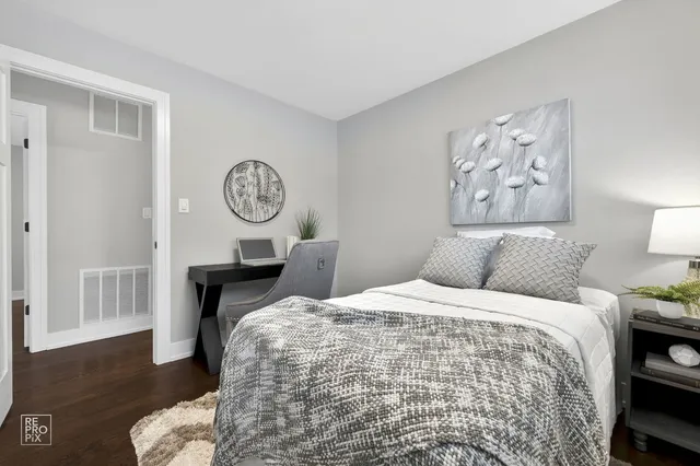 a bedroom with a bed and a lamp on dresser with wooden floor