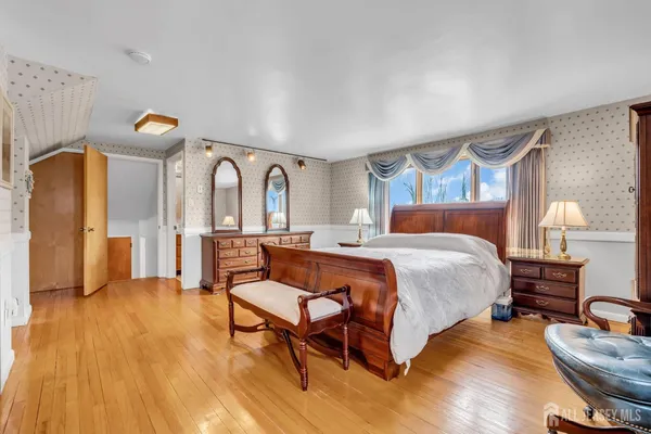 a spacious bedroom with a bed a dresser and wooden floor
