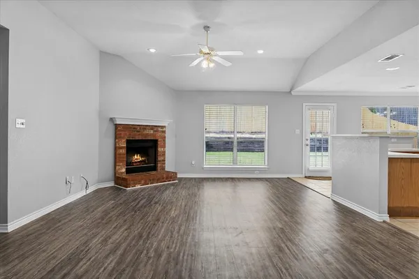 a view of an empty room with wooden floor fireplace and a window