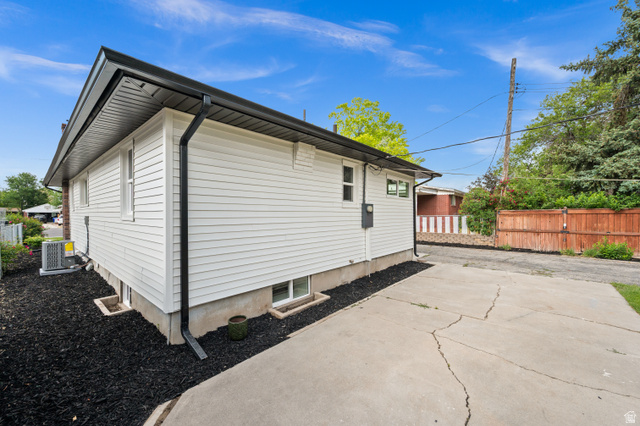 189 West Center Street Midvale, UT 84047 - Photo 58 of 64 White siding exterior with black gutters and downspouts, featuring a concrete driveway, basement windows, and dark ground cover