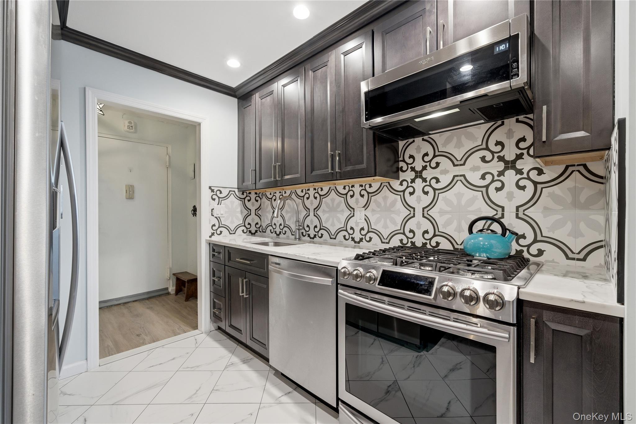 420 Shore Road, Unit 3M Long Beach, NY 11561 - Photo 5 of 23 Kitchen featuring stainless steel appliances, light marble finish flooring, light stone countertops, dark wood finish cabinets, and ornamental molding