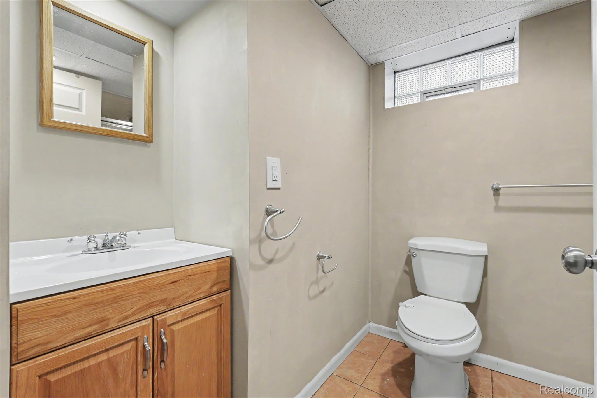 7136 Rosedale Boulevard Allen Park, MI 48101 - Photo 44 of 51 Wood-finish vanity with a white countertop and integrated sink, framed mirror, toilet, and glass block window